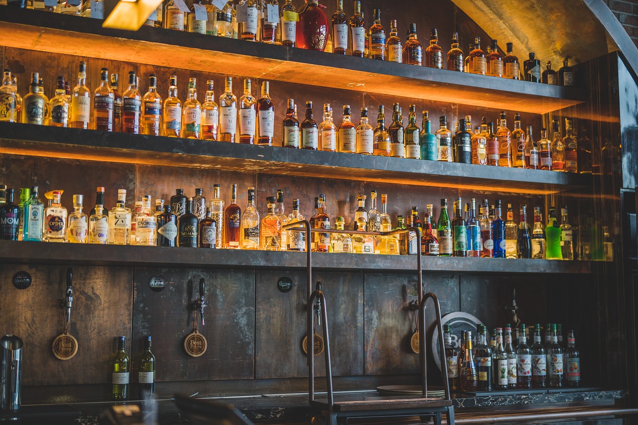 Fotografia de um bar todo em madeira com três prateleiras no qual estão várias bebidas expostas